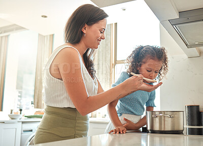 Buy stock photo Mother giving little daughter a wooden spoon to taste. Mother and daughter cooking together in the kitchen. Child tasting flavour in food