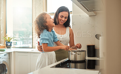 Buy stock photo Adorable little girl and her mother having fun while cooking together at home. Young mother standing behind her laughing daughter and helping her while stirring food on the stove. Mom and child preparing dinner together