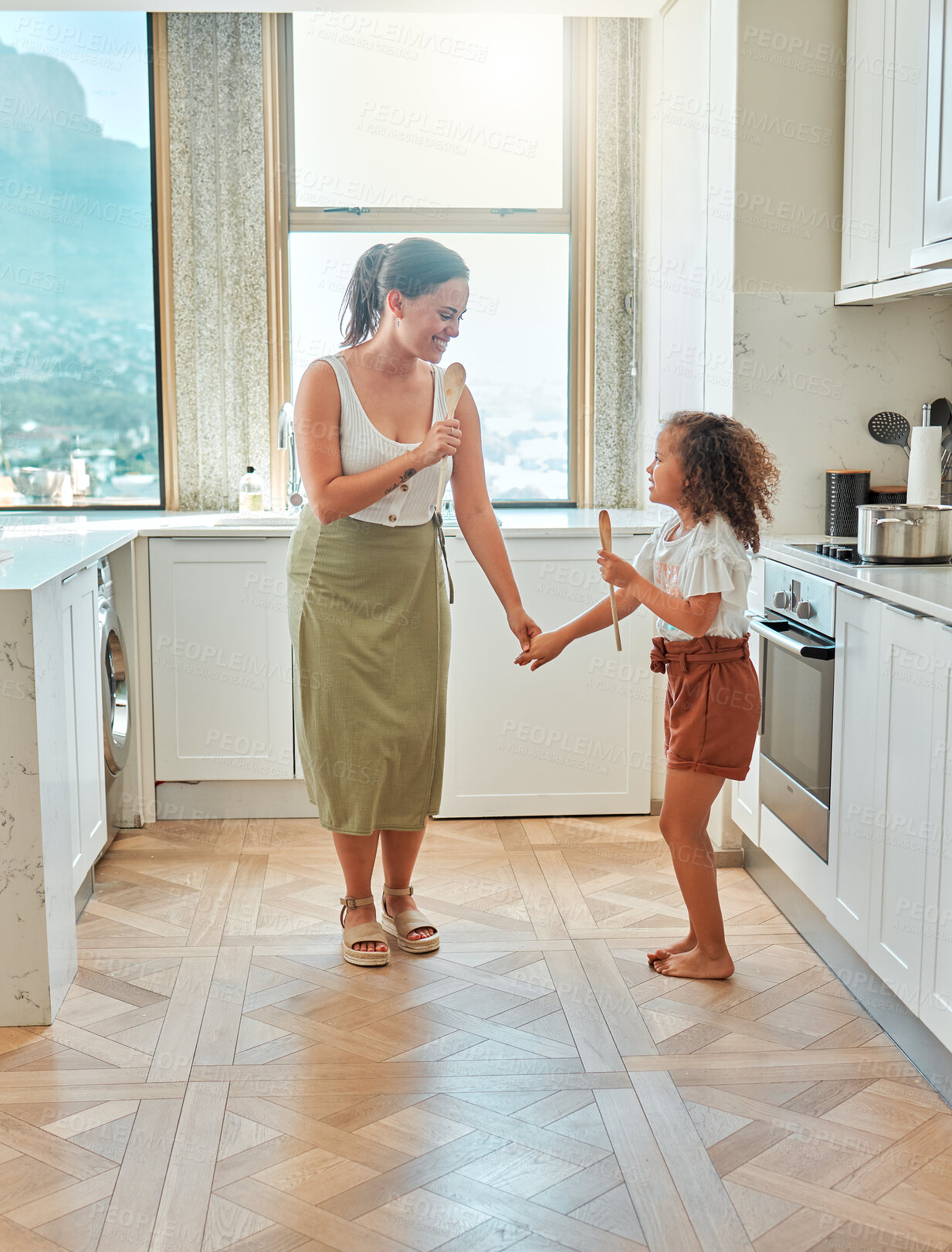 Buy stock photo Mother and little daughter singing and dancing in the kitchen. Mixed race mom and child holding wooden spoons while having fun at home