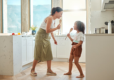 Buy stock photo Mother and little daughter singing karaoke and dancing in the kitchen. Mixed race mom and child holding wooden spoons while having fun during a sing-off at home