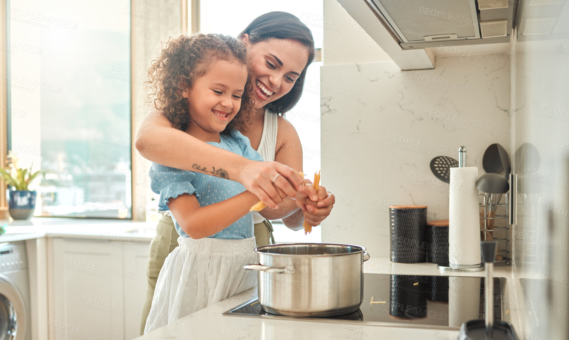 Buy stock photo Mother and little daughter cooking together in the kitchen. Mixed race mother and child standing by the stove breaking spaghetti and throwing it in boiling water