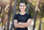 Fitness woman smiling at the camera while out for a run at the park. Cheerful female athlete standing with her arms crossed while exercising in nature