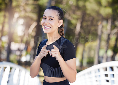Fitness woman smiling and pointing her index fingers at the camera while out for a run at the park. Cheerful female athlete motivating you to exercise and take care of your health