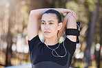 Portrait of a fit young hispanic woman wearing earphones and looking away while stretching her arms behind her head before a run. Female athlete warming up and getting ready for a cardio workout at park