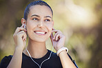 Close up of happy smiling young female athlete putting in earphones while exercising outdoors. Mixed race sportswoman listening to music during workout at park