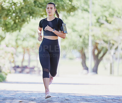 Sporty young female athlete wearing phone armband while jogging at park on a sunny day. Young hispanic woman running exercising outdoors