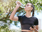 Young female athlete taking a break and drinking water from a bottle and holding smartphone while out for a run and exercising outdoors during the day