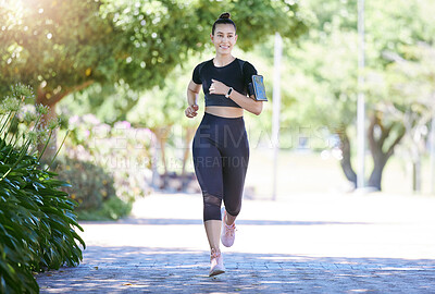 Happy sporty young female athlete wearing phone armband and smart watch while jogging at park on a sunny day. Young hispanic woman running exercising outdoors in nature