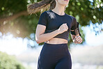 Close up of sporty young female athlete wearing armband while jogging at park on a sunny day. Young fit hispanic woman running exercising outdoors in nature