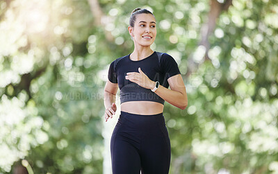 Happy young sporty female athlete wearing smart watch while jogging at park on a sunny day. Young hispanic woman running exercising outdoors in nature