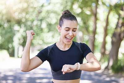 Cheerful young sporty female athlete celebrating while looking at smart watch. Hispanic sportswoman making winner gesture with clenched fist while tracking her progress while training outdoors