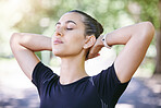 Close up of beautiful young hispanic sportswoman taking a break and looking relaxed while stretching her neck with her hands behind her head after a workout at the park