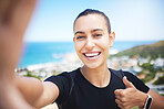 A fit young mixed race female jogger showing a thumbs up gesture outside while taking a selfie after a good exercise outdoors