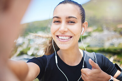 A fit young mixed race female jogger showing a thumbs up gesture outside while taking a selfie after a good exercise outdoors