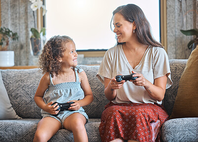 Hispanic mother and daughter playing video games together while sitting on the couch at home. Fun young mother and daughter using joysticks while playing and spending free time together on weekend