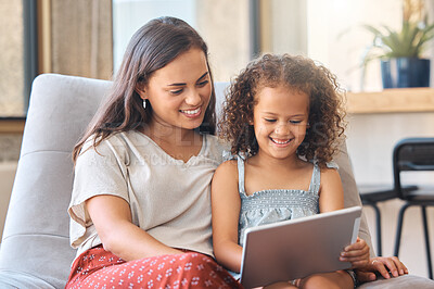 Happy little girl and loving mother sitting together on couch and using digital tablet to watch a movie or do a video call with family. Parent sitting with child while enjoying some online entertainment