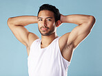 Handsome young hispanic man posing in studio isolated against a blue background. Mixed race male athlete wearing a vest and looking confident, healthy and fit. Exercising to increase his strength