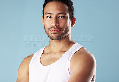 Handsome young hispanic man posing in studio isolated against a blue background. Mixed race male athlete wearing a vest and looking confident, healthy and fit. Exercising to increase his strength