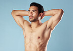 Handsome young hispanic man standing shirtless  in studio isolated against a blue background. Mixed race topless male athlete looking confident, healthy and fit. Exercising to increase his strength