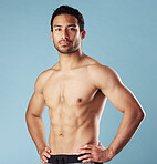 Handsome young hispanic man standing shirtless  in studio isolated against a blue background. Mixed race topless male athlete looking confident, healthy and fit. Exercising to increase his strength