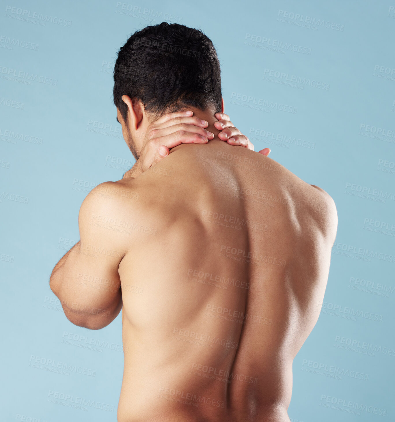 Buy stock photo Rearview young mixed race man standing shirtless in studio isolated against a blue background. Unrecognizable topless male athlete suffering from back pain or ache. He's picked up a fitness injury