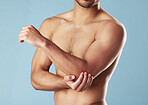 Closeup young mixed race man standing shirtless in studio isolated against a blue background. Unrecognizable topless male athlete suffering from an arm or elbow injury. Muscle cramp, ache or pain