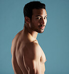 Handsome young hispanic man standing shirtless  in studio isolated against a blue background. Mixed race topless male athlete looking confident, healthy and fit. Exercising to increase his strength