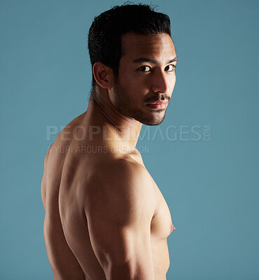 Buy stock photo Handsome young hispanic man standing shirtless  in studio isolated against a blue background. Mixed race topless male athlete looking confident, healthy and fit. Exercising to increase his strength