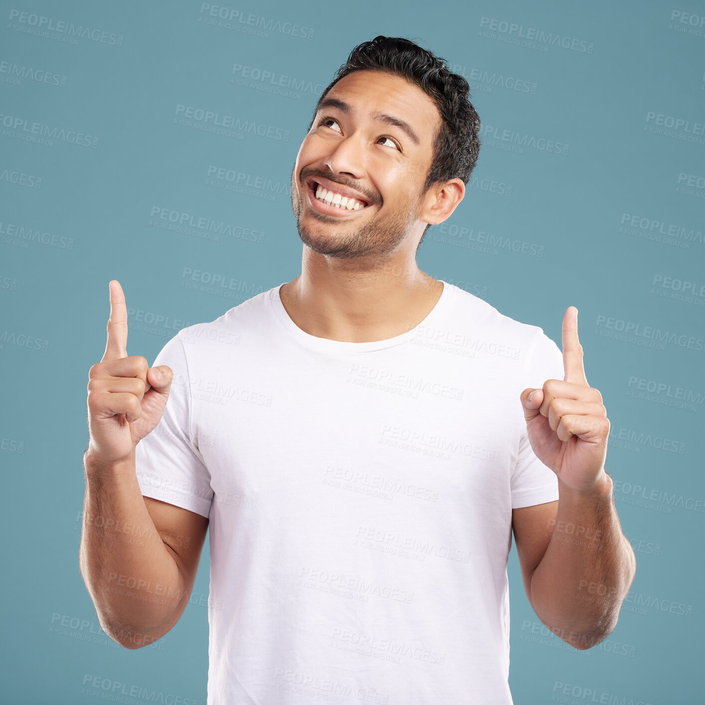 Buy stock photo Handsome young mixed race man pointing towards copyspace while standing in studio isolated against a blue background. Happy hispanic male advertising or endorsing your product, company or idea