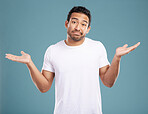 Handsome young mixed race man shrugging his shoulders while standing in studio isolated against a blue background. Confused hispanic male looking lost or clueless and making a, "So what?"  gesture