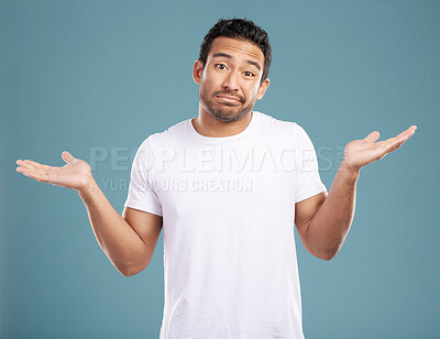 Handsome young mixed race man shrugging his shoulders while standing in studio isolated against a blue background. Confused hispanic male looking lost or clueless and making a, \