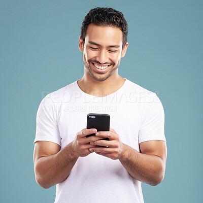 Handsome young mixed race man using his phone while standing in studio isolated against a blue background. Hispanic male sending a text message, using the internet online or browsing social media