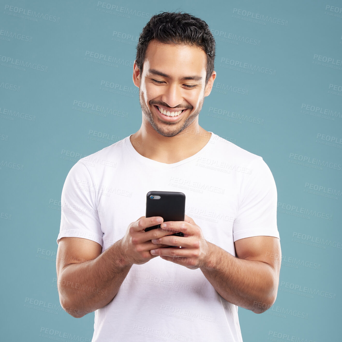 Buy stock photo Handsome young mixed race man using his phone while standing in studio isolated against a blue background. Hispanic male sending a text message, using the internet online or browsing social media