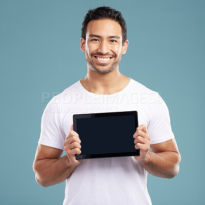 Buy stock photo Handsome young mixed race man holding his digital tablet while standing in studio isolated against a blue background. Hispanic male showing you a website or product on his wireless device screen