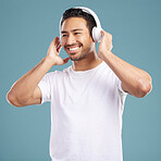 Handsome young mixed race man listening to music while standing in studio isolated against a blue background. Hispanic male streaming his favourite playlist online using wireless headphones