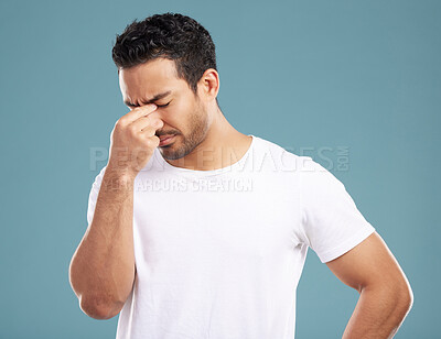 Buy stock photo Handsome young mixed race man suffering from a headache with his eyes closed while standing in studio isolated against a blue background. Hispanic male struggling with a migraine and feeling sick