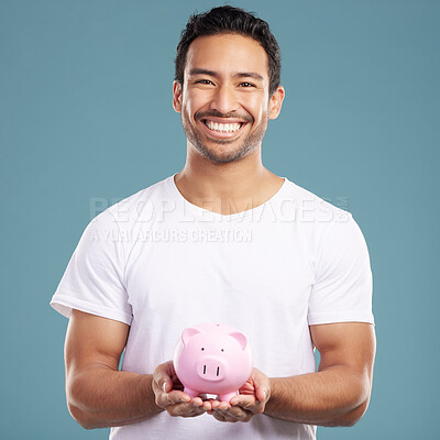 Buy stock photo Handsome young mixed race man holding his pink piggybank while standing in studio isolated against a blue background. Hispanic male showing savings, finance, investment, wealth management and banking