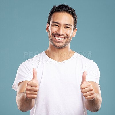 Handsome young mixed race man giving thumbs up while standing in studio isolated against a blue background. Hispanic male showing support or appreciation. Backing or endorsing a product or company