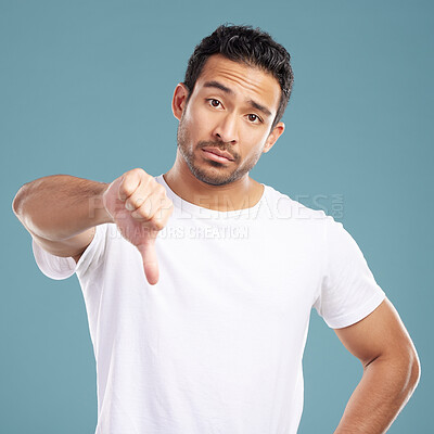 Buy stock photo Handsome young mixed race man giving thumbs down while standing in studio isolated against a blue background. Hispanic male showing disapproval or rejection. Feeling unimpressed, bad or negative