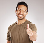 Handsome young mixed race man giving thumbs up while standing in studio isolated against a grey background. Hispanic male showing support or appreciation. Backing or endorsing a product or company