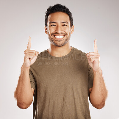 Buy stock photo Handsome young mixed race man pointing towards copyspace while standing in studio isolated against a grey background. Happy hispanic male advertising or endorsing your product, company or idea