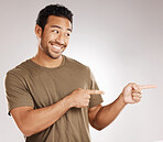 Handsome young mixed race man pointing towards copyspace while standing in studio isolated against a grey background. Happy hispanic male advertising or endorsing your product, company or idea