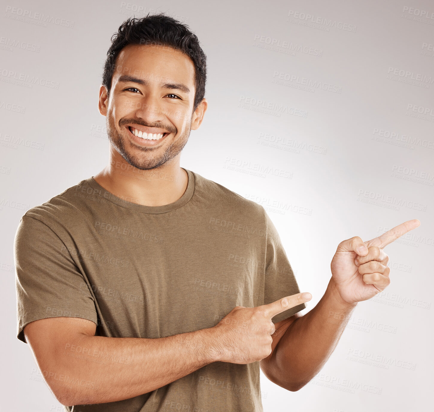 Buy stock photo Handsome young mixed race man pointing towards copyspace while standing in studio isolated against a grey background. Happy hispanic male advertising or endorsing your product, company or idea