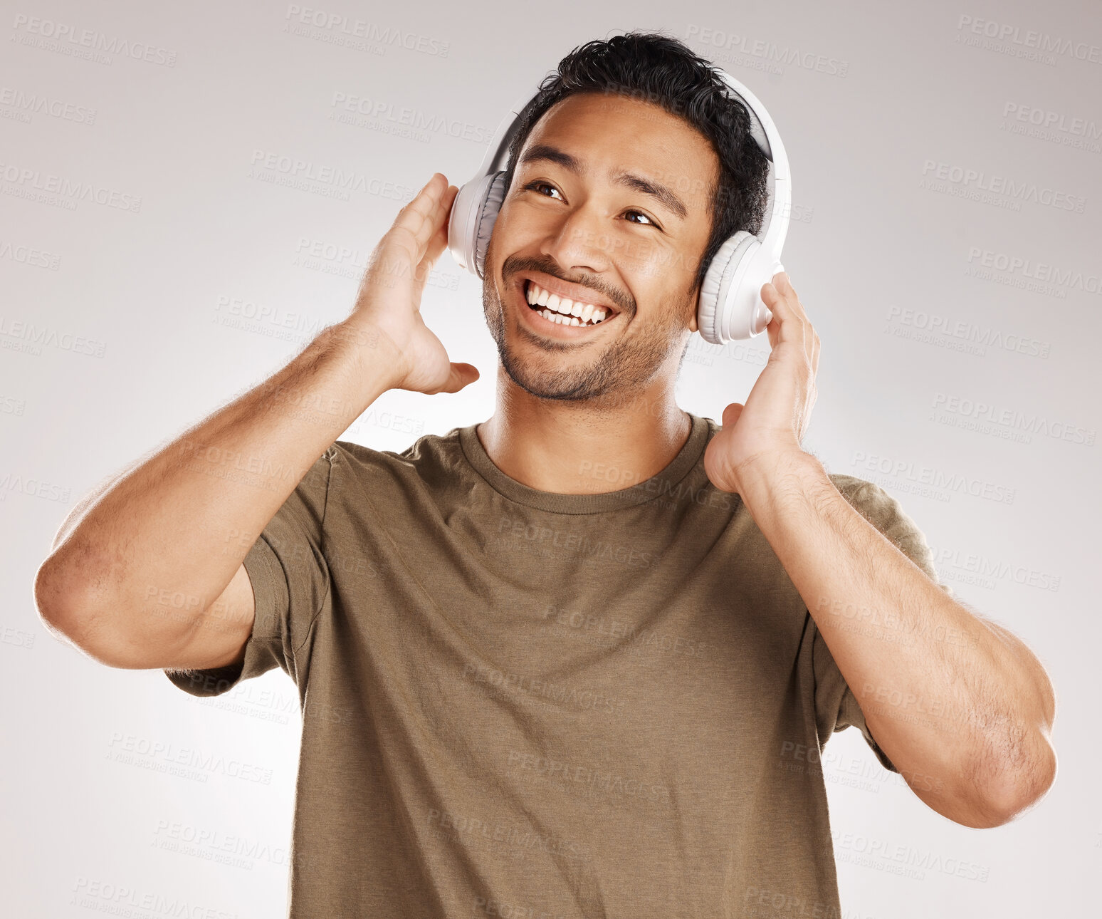 Buy stock photo Handsome young mixed race man listening to music while standing in studio isolated against a grey background. Hispanic male streaming his favourite playlist online using wireless headphones