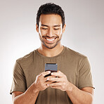 Handsome young mixed race man using his phone while standing in studio isolated against a grey background. Hispanic male sending a text message, using the internet online or browsing social media