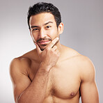 Handsome young mixed race man touching his face and posing shirtless isolated in studio against a grey background. Hispanic well groomed male looking confident and happy with his daily skincare regime