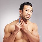 Handsome young mixed race man shirtless in studio isolated against a grey background. Hispanic male in pain after cutting himself while shaving. Take care when you groom or shave your beard and face