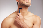 Closeup young mixed race man shirtless in studio isolated against a grey background. Hispanic male using a razor while shaving. Take care of your skin when you groom or shave your beard and face