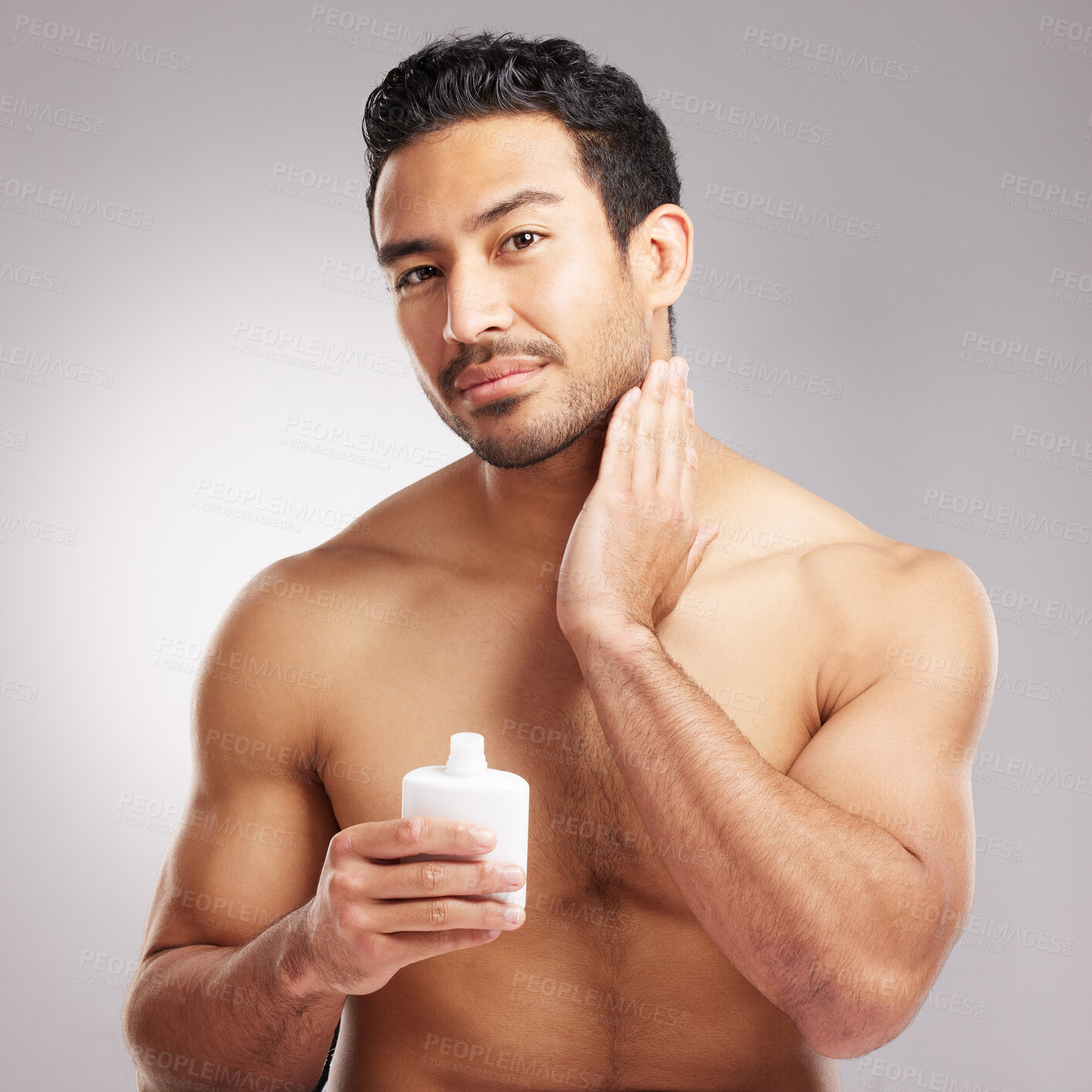 Buy stock photo Handsome young mixed race man shirtless in studio isolated against a grey background. Hispanic male applying aftershave after shaving. Take care of your skin when you groom or shave your beard and face