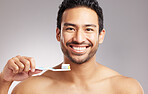 Closeup young mixed race man shirtless in studio isolated against a grey background. Hispanic male brushing his teeth. Taking caring of mouth and oral hygiene to promote dental health and healthy gums